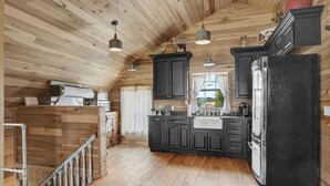 A spacious kitchen with wooden floors, black cabinets, and a large refrigerator. - TimberRose B&B (Fredericksburg)