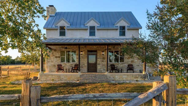 A two-story stone house with a metal roof, a front porch with four wooden chairs, and a stone staircase leading to the entrance. - TimberRose B&B (Fredericksburg)
