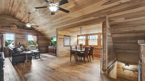A spacious cabin with a dining area, a living room with a sofa and a fireplace, and a kitchen visible through an open doorway. - TimberRose B&B (Fredericksburg)