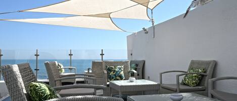 Una terraza con mobiliario de mimbre, una mesa de vidrio y vistas al mar.