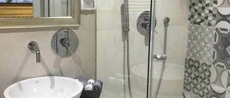 Un baño moderno con cabina de ducha acristalada, un lavabo blanco y baldosas estampadas.