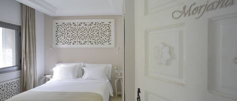 A bedroom with a bed, a nightstand, a decorative wall panel, and a door with the name 'Morjana'.
