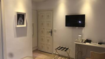 A hotel room with a bed, a desk with a computer, a TV mounted on the wall, a chair, and a door with a decorative pattern.