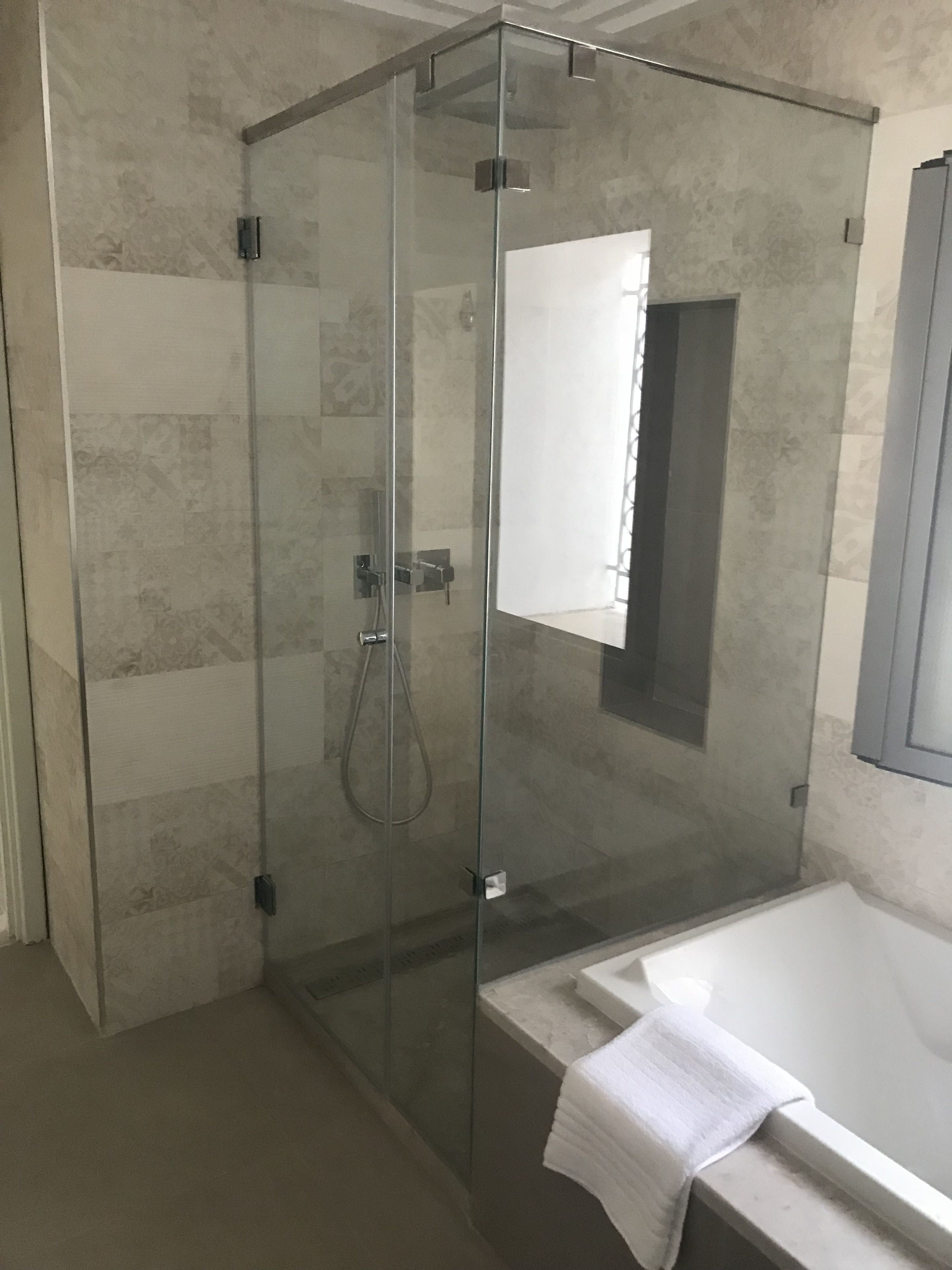A modern bathroom with a glass-enclosed shower, a white bathtub, and a towel hanging on the tub.