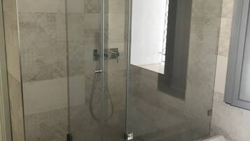 A modern bathroom with a glass-enclosed shower, a white bathtub, and a towel hanging on the tub.
