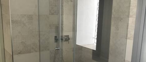 Een moderne badkamer met een douchecabine van glas, een wit bad en een handdoek aan de badrand.