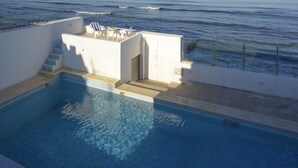 A pool area with a view of the ocean, a small seating area with chairs and a table, and a staircase leading to a higher level. - Dar Corniche La Marsa - Adults Only (La Marsa)