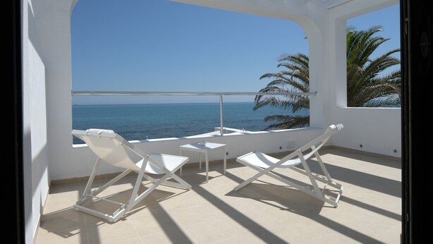 A balcony with white chairs and a table, overlooking a clear blue sea and palm trees. - Dar Corniche La Marsa - Adults Only (La Marsa)