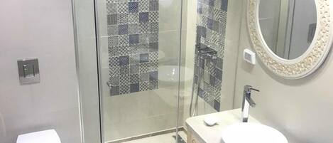 A modern bathroom with a glass shower enclosure, a white toilet, and a vanity with two sinks.