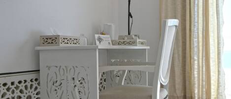 A white, intricately designed desk with a chair, a flat-screen TV mounted on the wall, and a floor lamp.