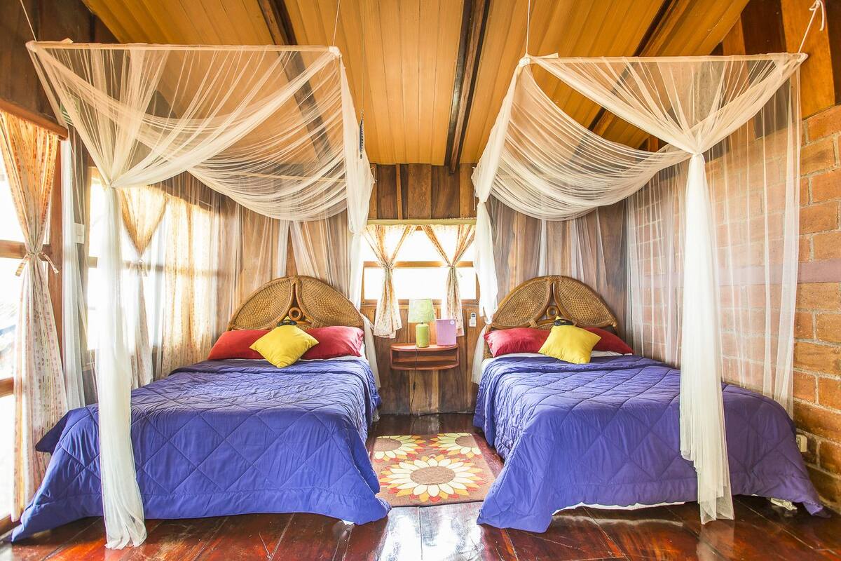 A room with two beds, each with a canopy, wooden headboards, and colorful bedding.
