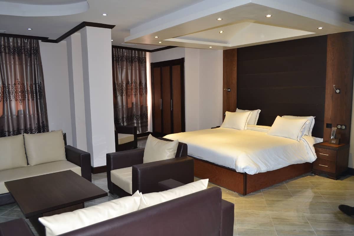 A modern hotel room with a large bed, a sofa, a coffee table, and a nightstand.