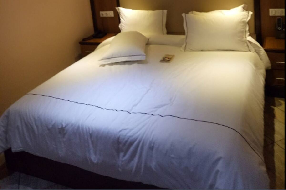 A neatly made bed with white linens and pillows, a framed picture on the wall above, and a ceiling light fixture.