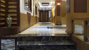 A hotel lobby with marble flooring, wooden paneling, and a chandelier. - Assala (Oran)