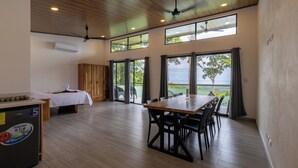 A spacious room with a wooden ceiling, a dining table with chairs, a bed, and large windows with curtains. - Casa Odi-SEA - Portasol Vacation Rentals (Savegre)