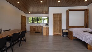 A modern interior with a wooden dining table, chairs, a kitchen area, and a bed. - Casa Odi-SEA - Portasol Vacation Rentals (Savegre)