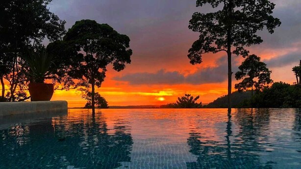 A swimming pool with clear water reflecting the sunset and surrounding trees. - Casa Odi-SEA - Portasol Vacation Rentals (Savegre)