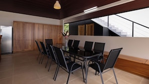 A modern kitchen with a dining table and chairs, wooden cabinets, and a staircase leading to an upper level. - Casa Odi-SEA - Portasol Vacation Rentals (Savegre)