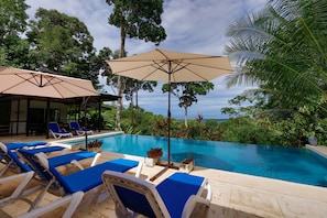 A poolside area with lounge chairs, umbrellas, and a view of the ocean. - Casa Odi-SEA - Portasol Vacation Rentals (Savegre)