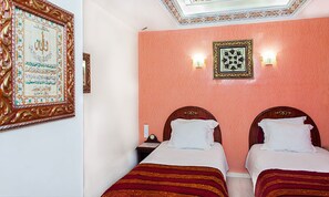 A hotel room with two beds, a nightstand, and a wall with decorative frames. - Dar Diaf Bouchaoui (Algiers)