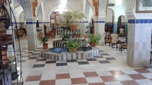 Un vestíbulo con piso a cuadros, plantas en macetas y una fuente.