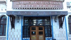 Fachada de hotel con un letrero en idioma extranjero, una puerta de madera grande y azulejos decorativos azules y blancos.