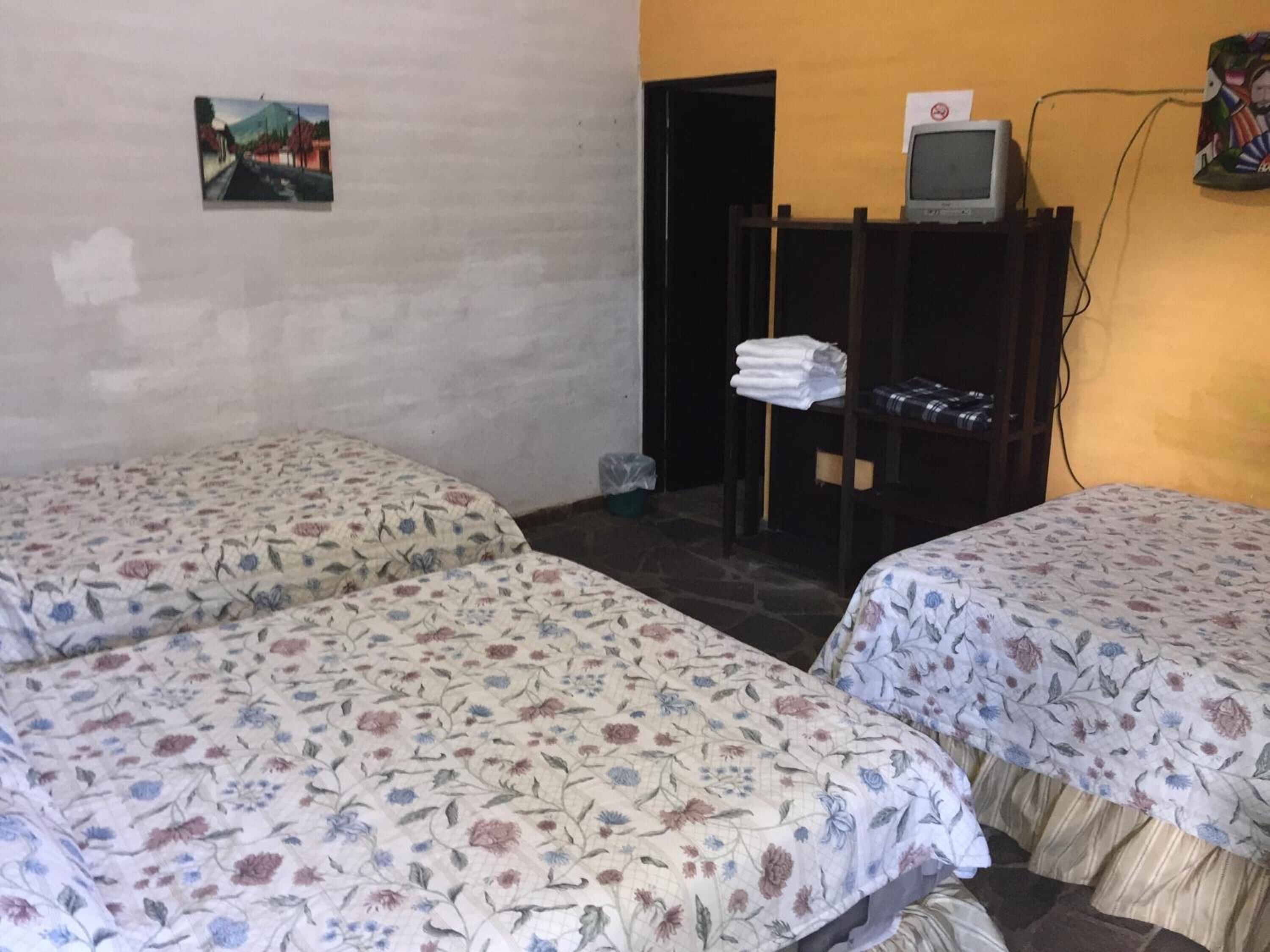 A room with two beds, a television on a stand, and a door leading to another room.