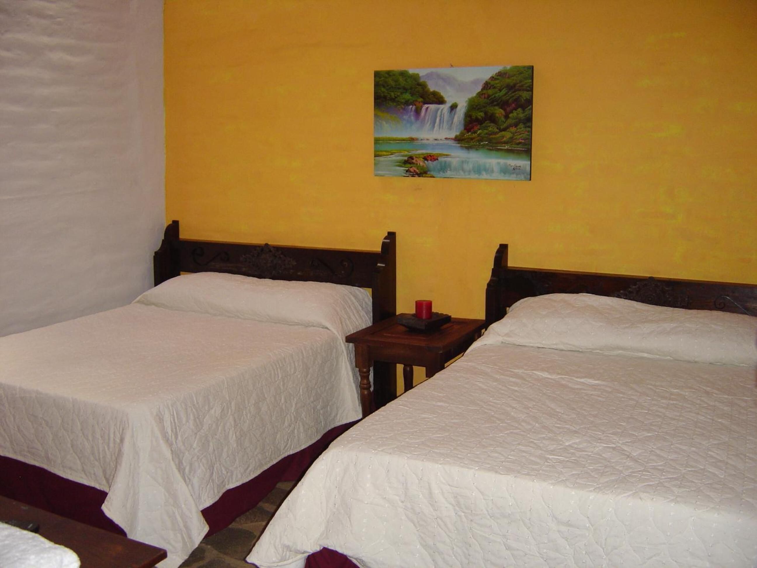 A room with two single beds, a nightstand with a red candle, and a painting of a waterfall on the wall.