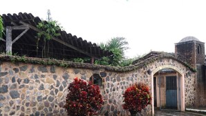 A stone wall with a rustic archway leading to a door, surrounded by greenery and a cobblestone street. - Hotel Villa Santo Domingo (Concepcion de Ataco)