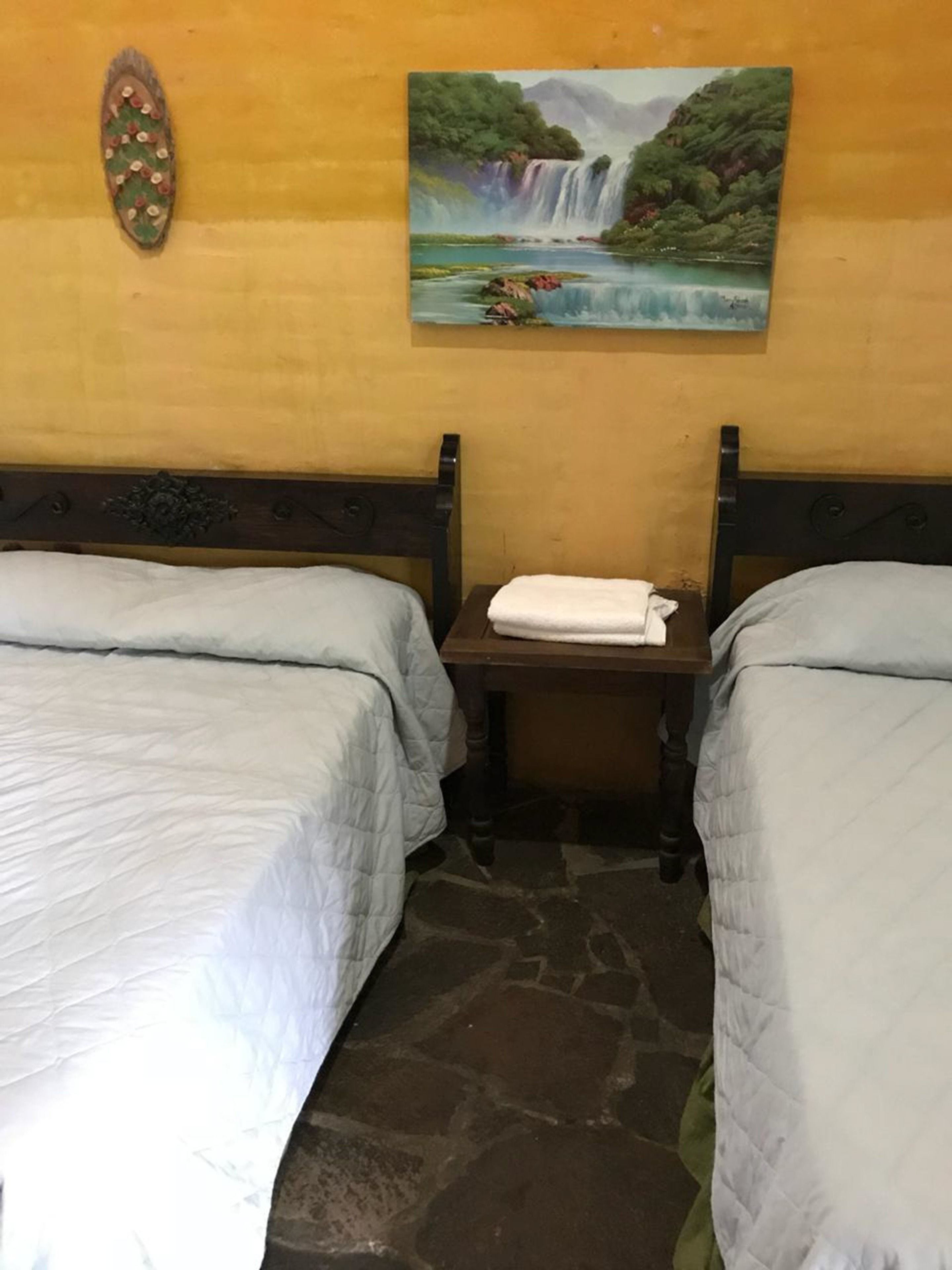 A room with two beds, a nightstand, and a painting of a waterfall.