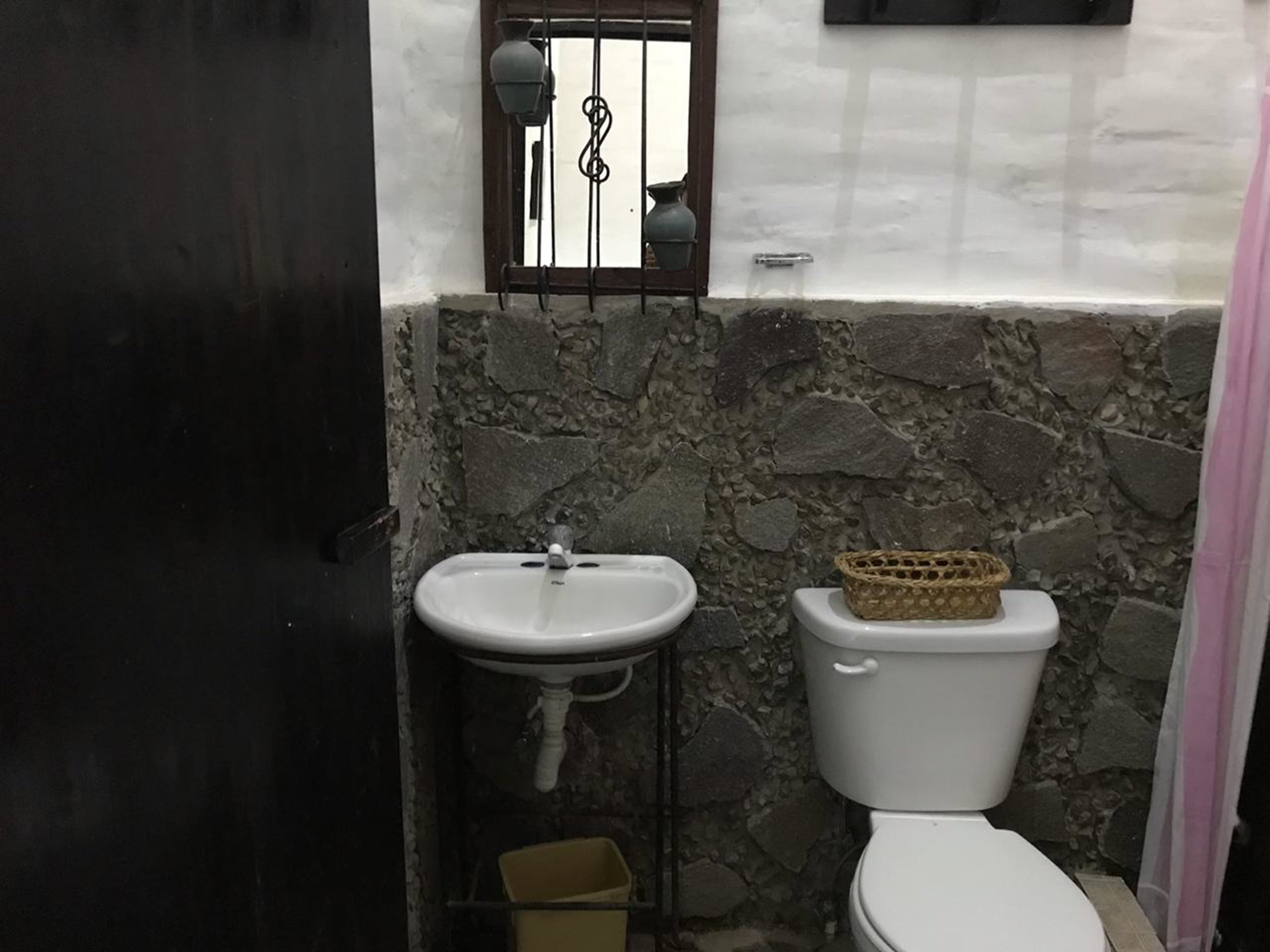Ein Badezimmer mit Steinwand, Waschbecken in Weiß und Toilette.