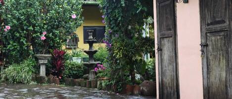 Une cour avec un chemin de pierre, une fontaine et une végétation luxuriante.