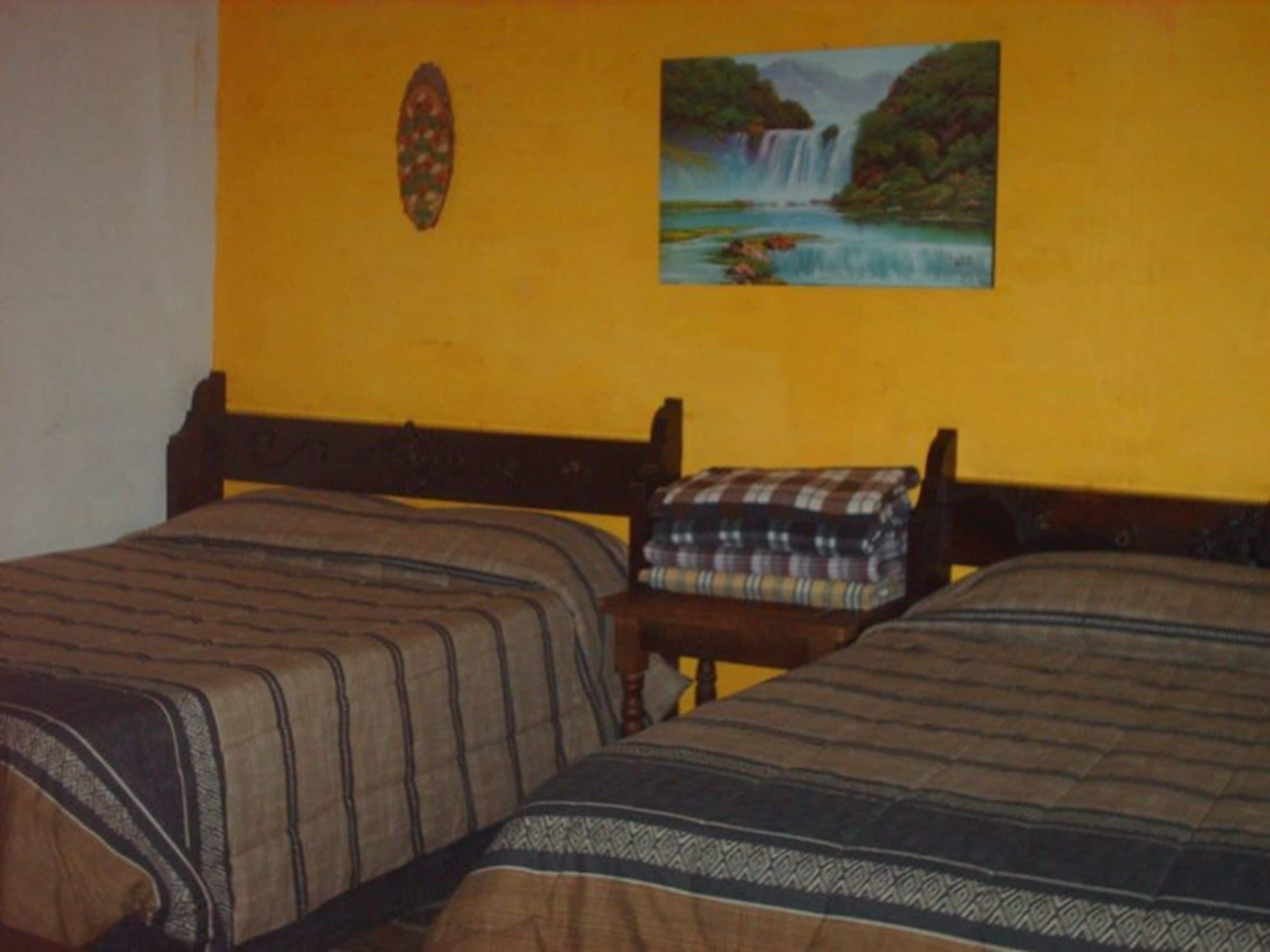 Ein Zimmer mit zwei Betten, einem kleinen Tisch und einem Bild an der Wand.