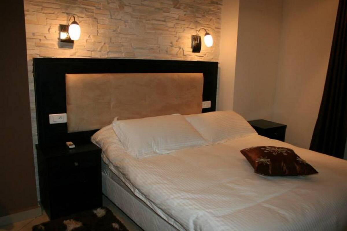 Ein Schlafzimmer mit Stehwand, einem Kopfteil, zwei Nachttischlampen, einem Bett mit weißer Bettwäsche und einem braunen Kissen.