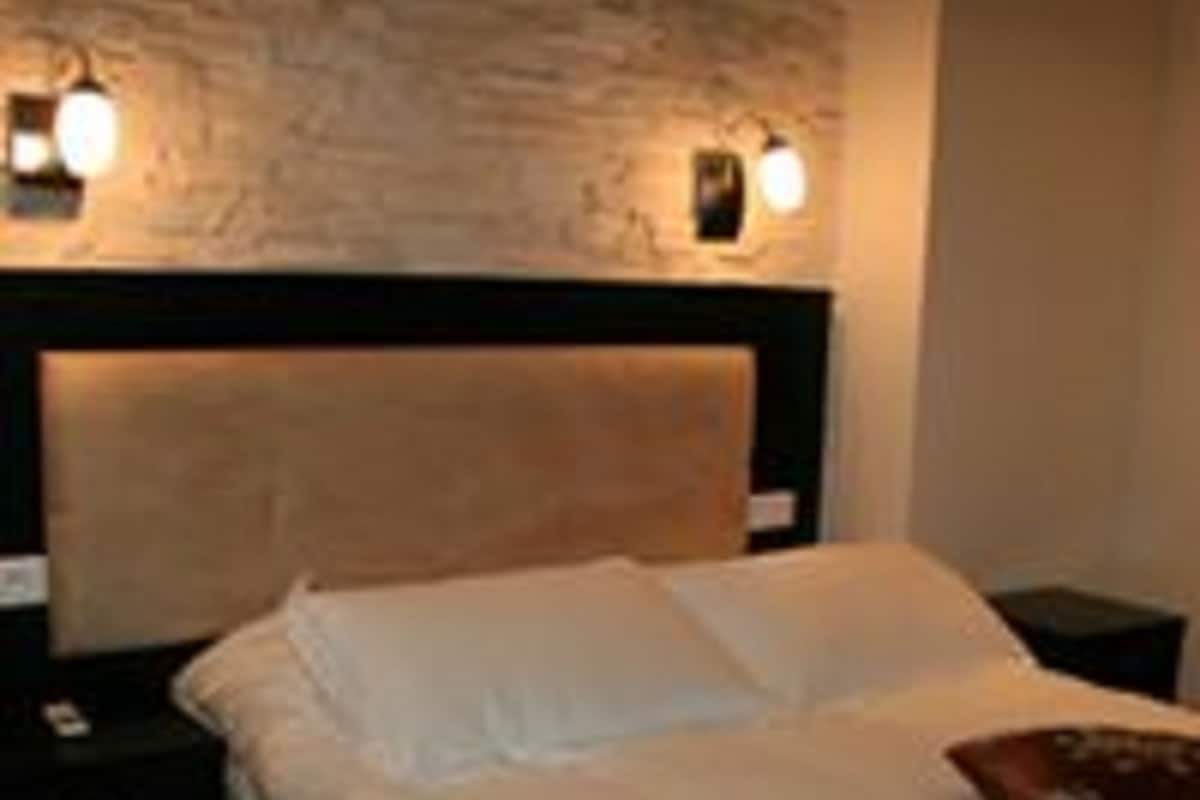 Ein ordentlich bezogenes Bett mit weißen Leinen in einem Zimmer mit Steinwand und zwei Wandleuchten.