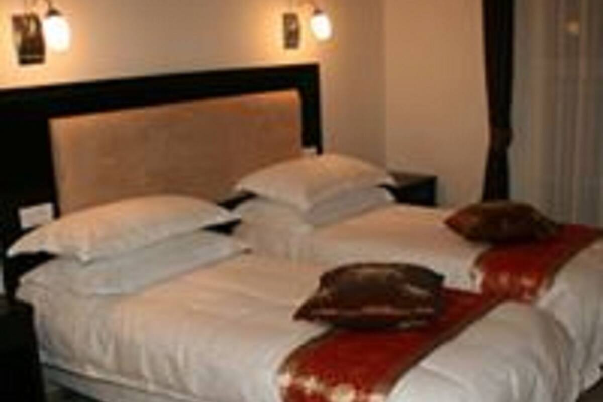 Ein Doppelbett mit weißer Bettwäsche und einer roten Tagesdecke, zwei Nachttische und Wandleuchten zum Lesen.