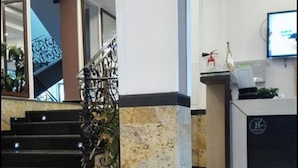 A hotel lobby with a marble staircase, a reception desk, and a monitor on the wall. - Hotel 2 Horloges (Oran)