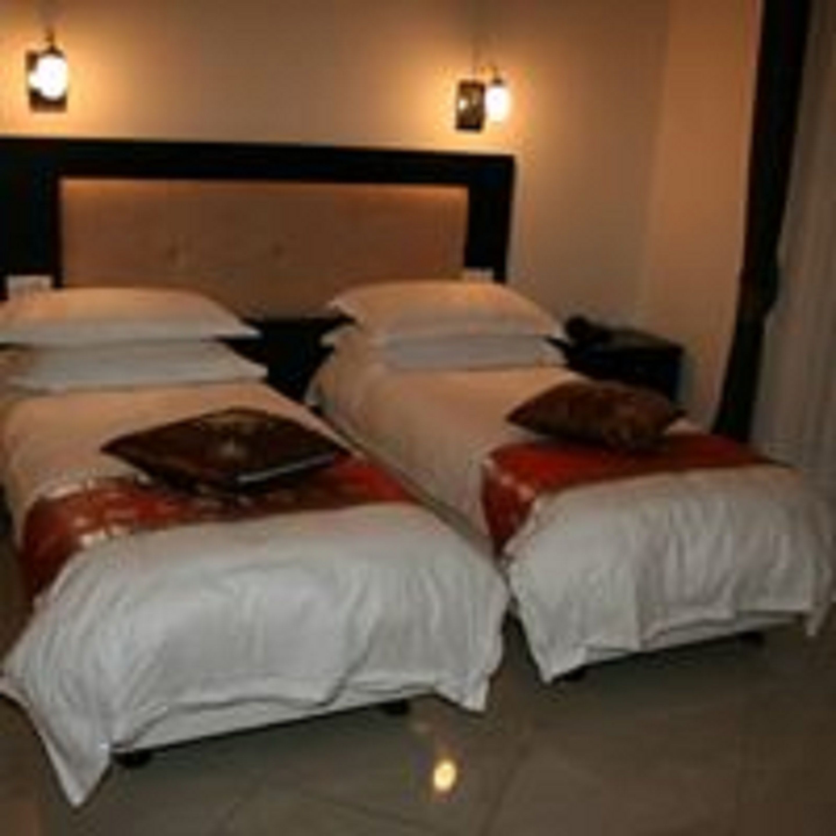 A hotel room with two single beds, a nightstand, and a wall-mounted lamp.