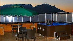 A rooftop terrace with a hot tub, a table with chairs, and a view of a mountain. - Hotel 2 Horloges (Oran)