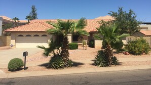A residential house with a red-tiled roof, a garage, and a well-maintained front yard with palm trees and shrubs. - Downtown PHX -Private Home/Fam. Friendly/4 Blocks/Convention Center/Chase Field (Phoenix)