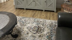 A living room with a flat-screen TV mounted above a light gray cabinet with decorative cutouts. A patterned rug is on the wooden floor, and there is a round table with a metal base. - Downtown PHX -Private Home/Fam. Friendly/4 Blocks/Convention Center/Chase Field (Phoenix)
