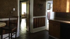 A kitchen with wooden cabinets, a dining area with a chair, and a hallway leading to another room.
