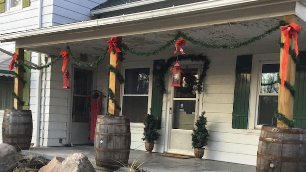 A house with a porch decorated with Christmas garlands and red bows, large wooden barrels, and potted plants.