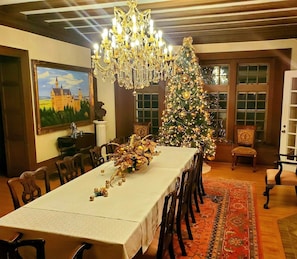 Une salle à manger avec une longue table, un lustre somptueux et un sapin de Noël.