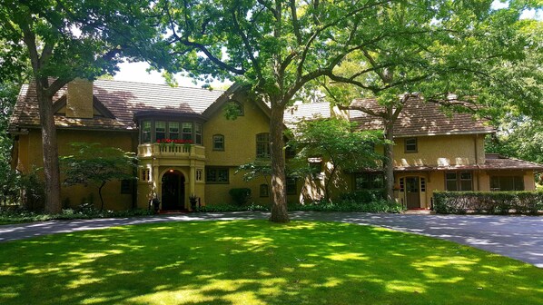 A two-story house with a balcony, a front entrance, and a well-maintained lawn. - Beautiful Historic Tudor Mansion with sandy Private Beach (Oconomowoc)