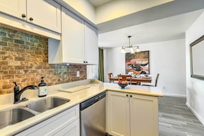 Modern kitchen with double sink, stainless steel dishwasher, and brick backsplash.