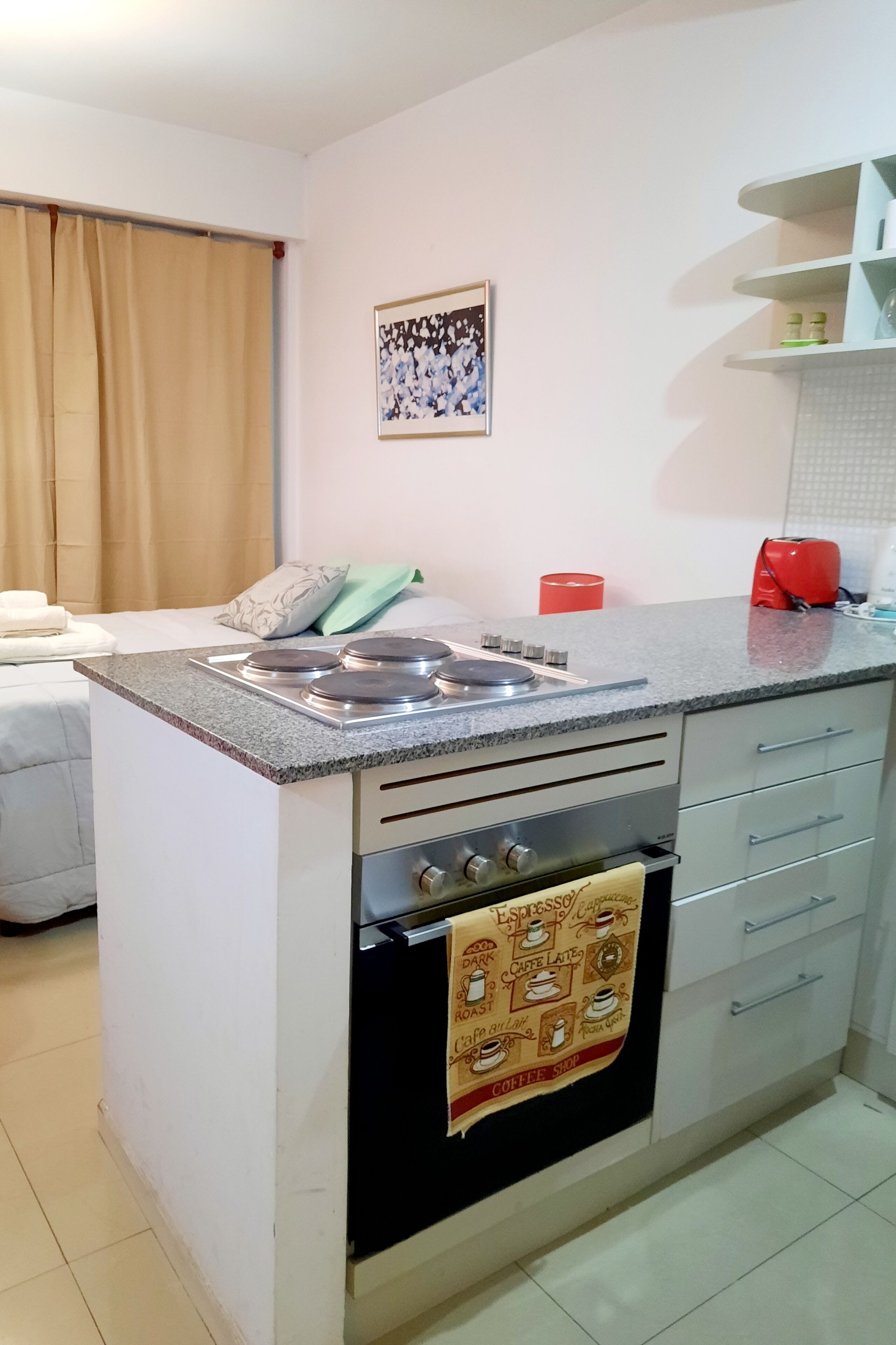 A compact kitchen with a gas stove, oven, and a coffee shop-themed towel.