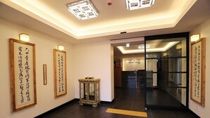 A hallway with traditional Japanese calligraphy on the walls, a small ornate table, and a reception area with a glass door. - Namyangju Bukhangang Dolce Casa Hotel (Namyangju)