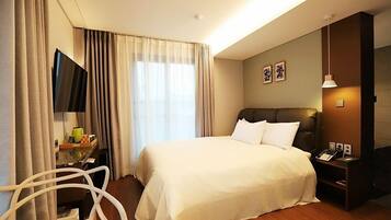 Habitación de hotel con una cama grande, un escritorio con silla, un televisor de pantalla plana y una mesita de noche con lámpara.