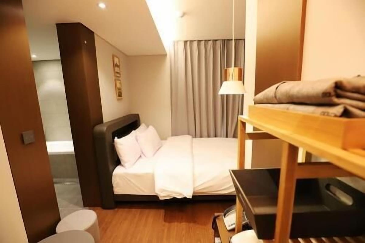 A hotel room with a bed, a desk, a lamp, and a wardrobe.